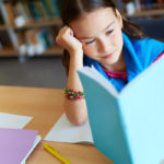 Portrait of a lovely girl sitting by the desk and reading