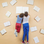 Happy children are reading book on the floor with group of books around them