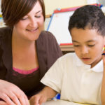 Primary school teacher helping boy learn numbers
