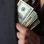 Close up of a business mans hand hiding money in his suit jacket pocket.