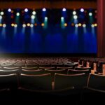 empty seat in vintage auditorium or theater with lights on stage.
